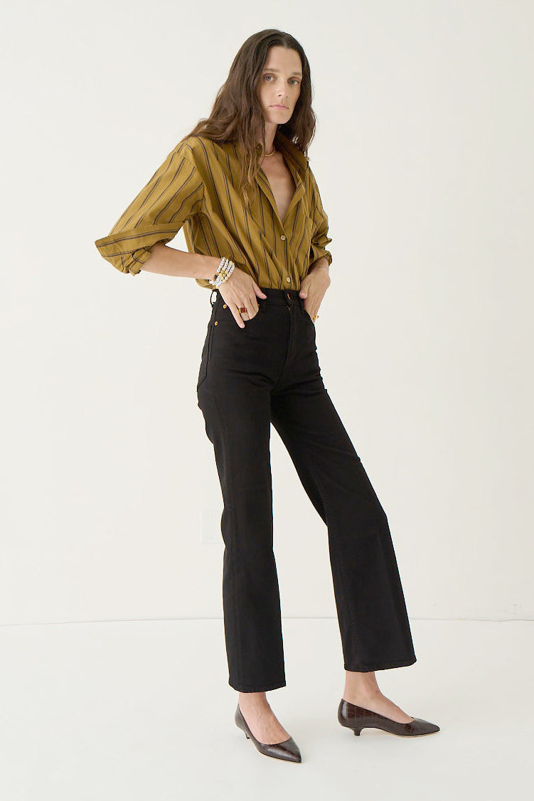 A woman modeling a mustard yellow and olive green striped button-down shirt with black cropped flare jeans and dark brown pointed-toe flats, standing against a plain white studio background.