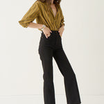 A woman modeling a mustard yellow and olive green striped button-down shirt with black cropped flare jeans and dark brown pointed-toe flats, standing against a plain white studio background.