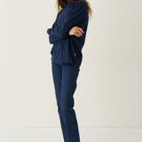 A woman modeling a matching navy blue lounge set consisting of a long-sleeve sweatshirt and straight-leg jeans, paired with black shoes, against a plain white studio background.