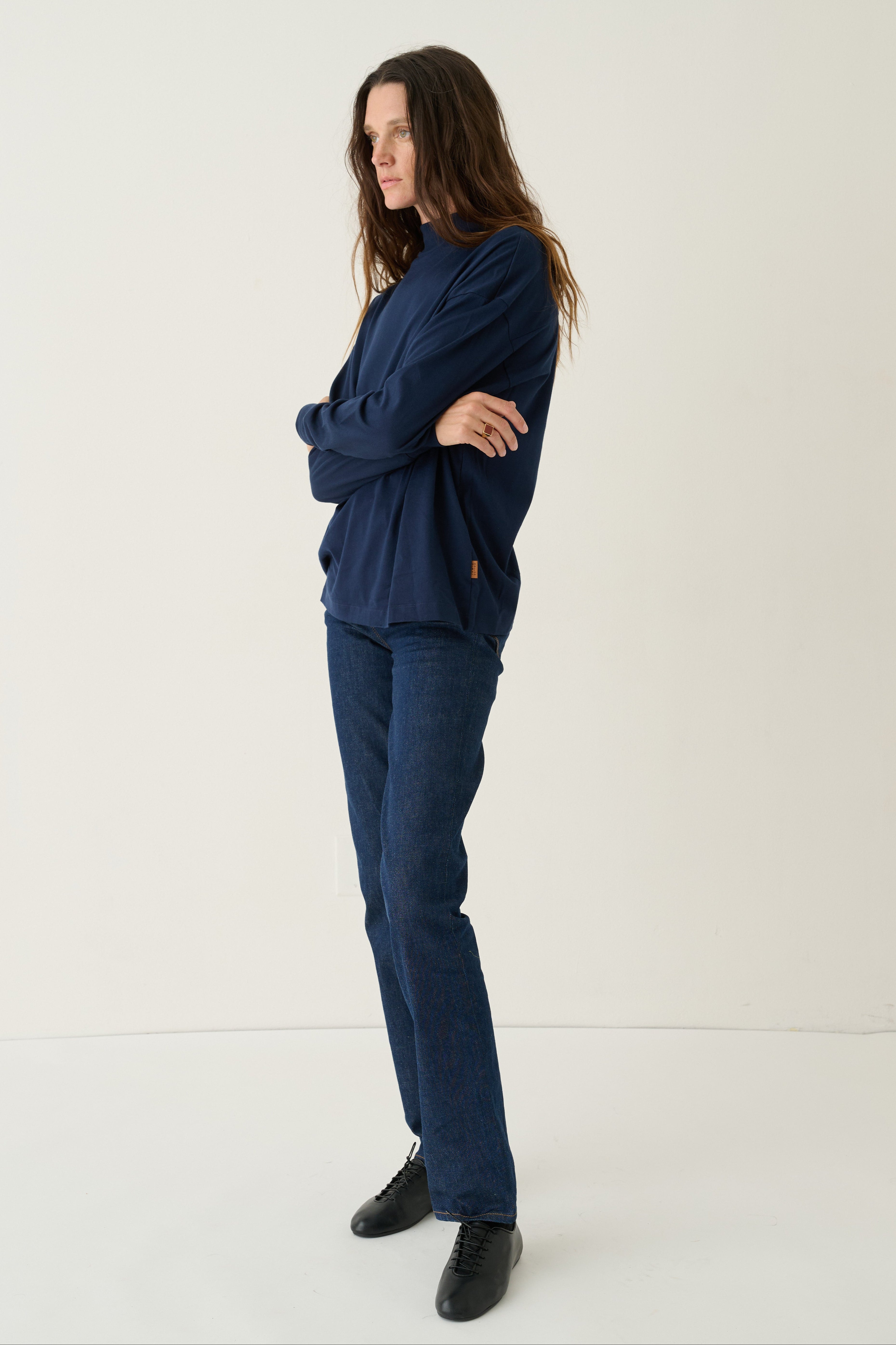A woman modeling a matching navy blue lounge set consisting of a long-sleeve sweatshirt and straight-leg jeans, paired with black shoes, against a plain white studio background.