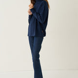 A woman modeling a navy blue long-sleeve top and matching navy blue jeans against a plain off-white studio background.