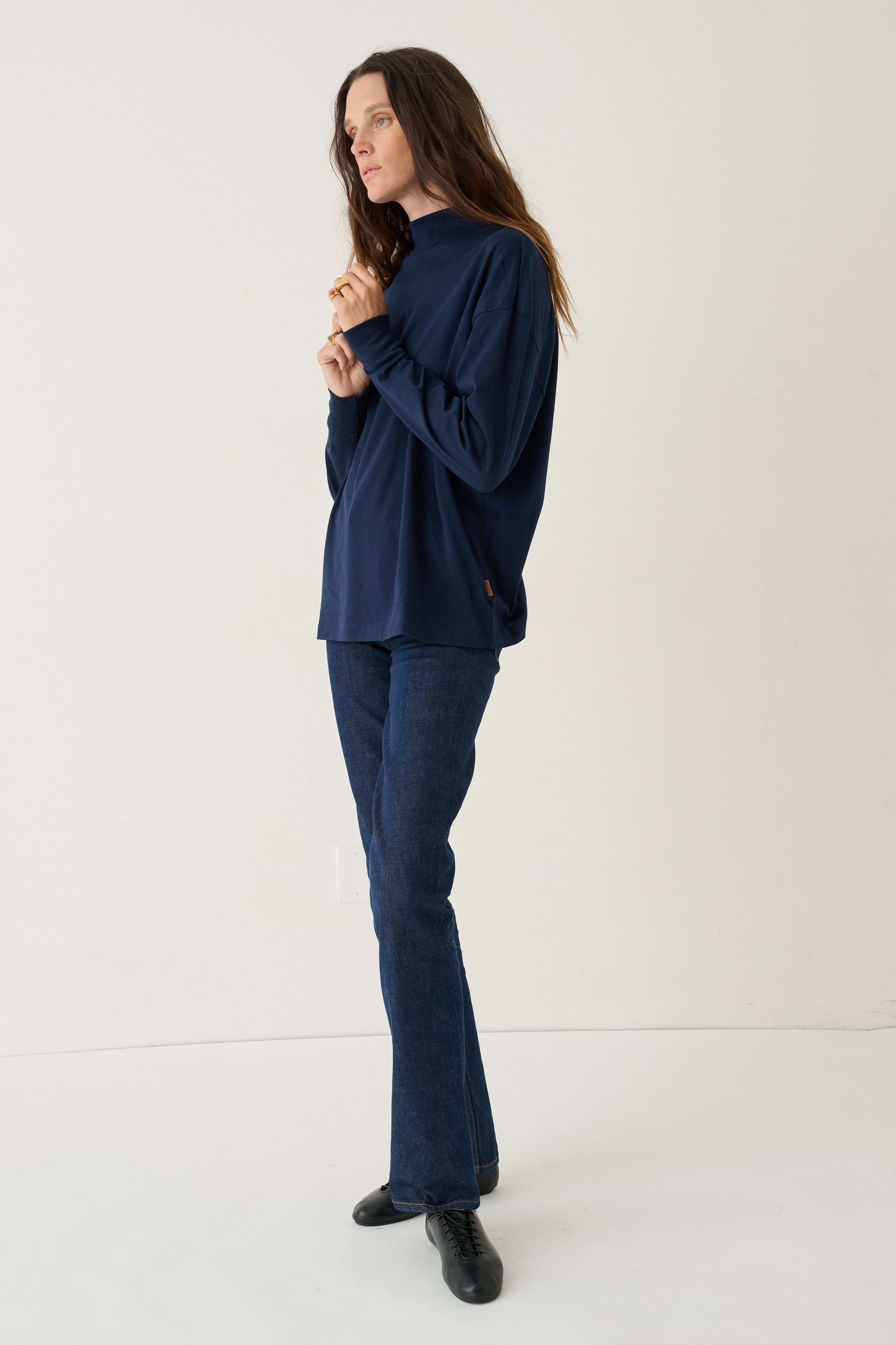 A woman modeling a navy blue long-sleeve top and matching navy blue jeans against a plain off-white studio background.
