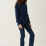 A woman modeling a matching navy blue sweatshirt and straight-leg jeans set, paired with black shoes, against a plain white studio background.