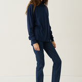 A woman modeling a matching navy blue sweatshirt and straight-leg jeans set, paired with black shoes, against a plain white studio background.