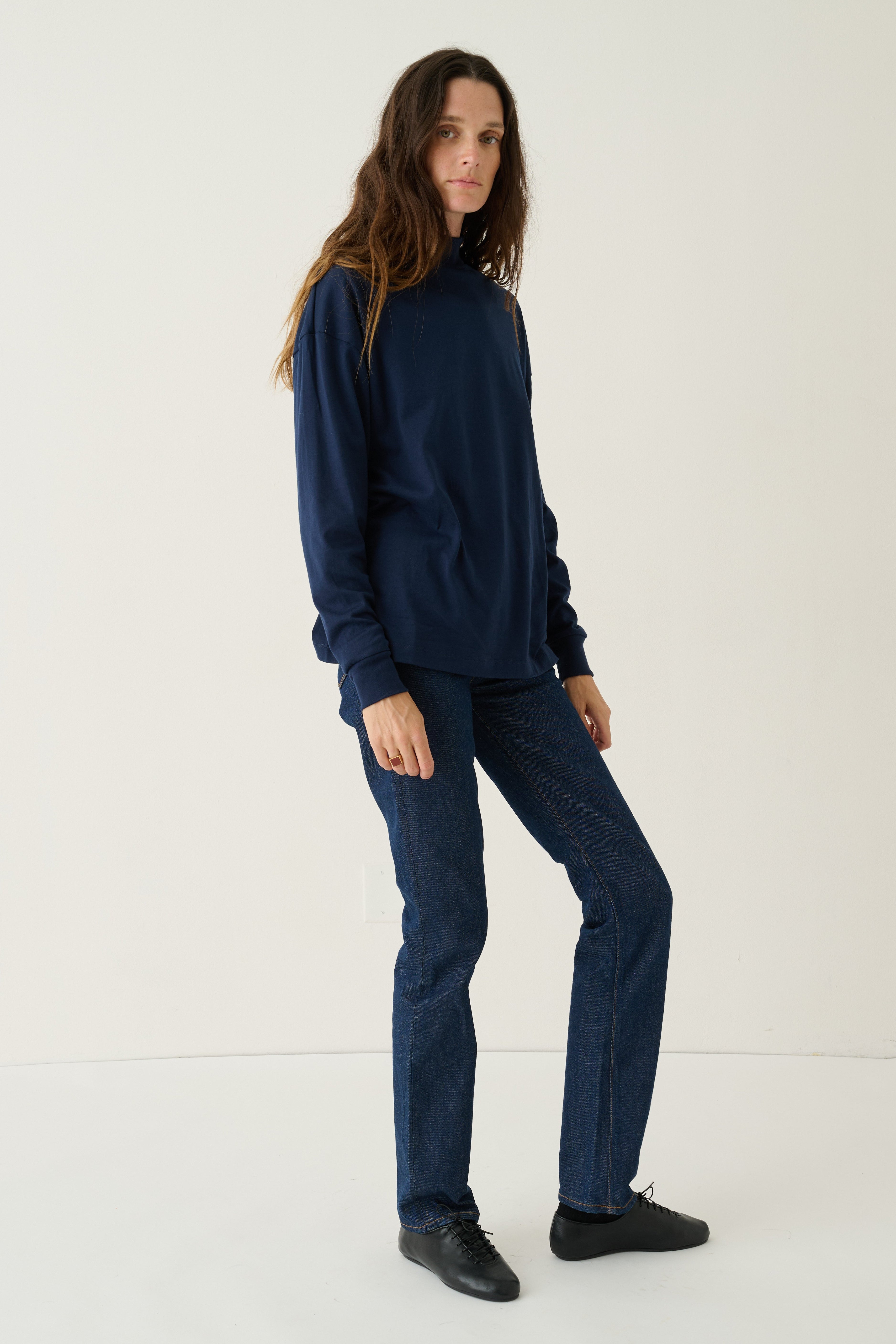 A woman modeling a matching navy blue sweatshirt and straight-leg jeans set, paired with black shoes, against a plain white studio background.