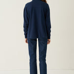 A woman viewed from behind wearing a matching navy blue long-sleeve top and trousers set, standing against a plain off-white studio background.