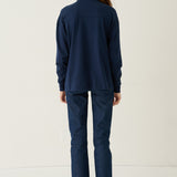 A woman viewed from behind wearing a matching navy blue long-sleeve top and trousers set, standing against a plain off-white studio background.