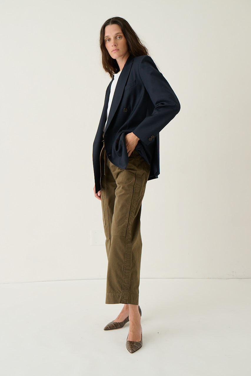 A woman modeling a navy blue double-breasted blazer, olive green cropped trousers, a white top, and brown pointed-toe flats against a plain white studio background.