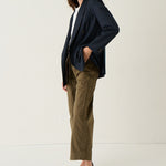 A woman modeling a navy blue double-breasted blazer, olive green cropped trousers, a white top, and brown pointed-toe flats against a plain white studio background.