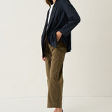 A woman modeling a navy blue double-breasted blazer, olive green cropped trousers, a white top, and brown pointed-toe flats against a plain white studio background.