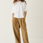 A woman modeling a white short-sleeve t-shirt and loose, wide-leg brown pants against a plain, light beige studio background.