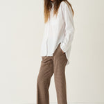 A woman modeling a white long-sleeve button-up shirt and brown houndstooth cropped trousers with burgundy pointed-toe flats, set against a plain off-white studio background.
