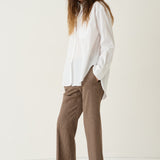A woman modeling a white long-sleeve button-up shirt and brown houndstooth cropped trousers with burgundy pointed-toe flats, set against a plain off-white studio background.