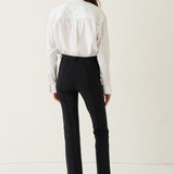 A model shown from the back wearing a white long-sleeve blouse and black trousers, standing against a plain off-white studio background.