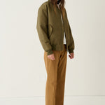 A model stands in a studio wearing an olive green bomber jacket over a white top, paired with brown wide-leg pants and tan pointed-toe flats.