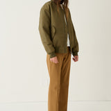 A model stands in a studio wearing an olive green bomber jacket over a white top, paired with brown wide-leg pants and tan pointed-toe flats.