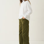 A woman modeling a white long-sleeve top and olive green wide-leg pants against a plain white studio background.