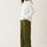 A woman modeling a white long-sleeve top and olive green wide-leg pants against a plain white studio background.