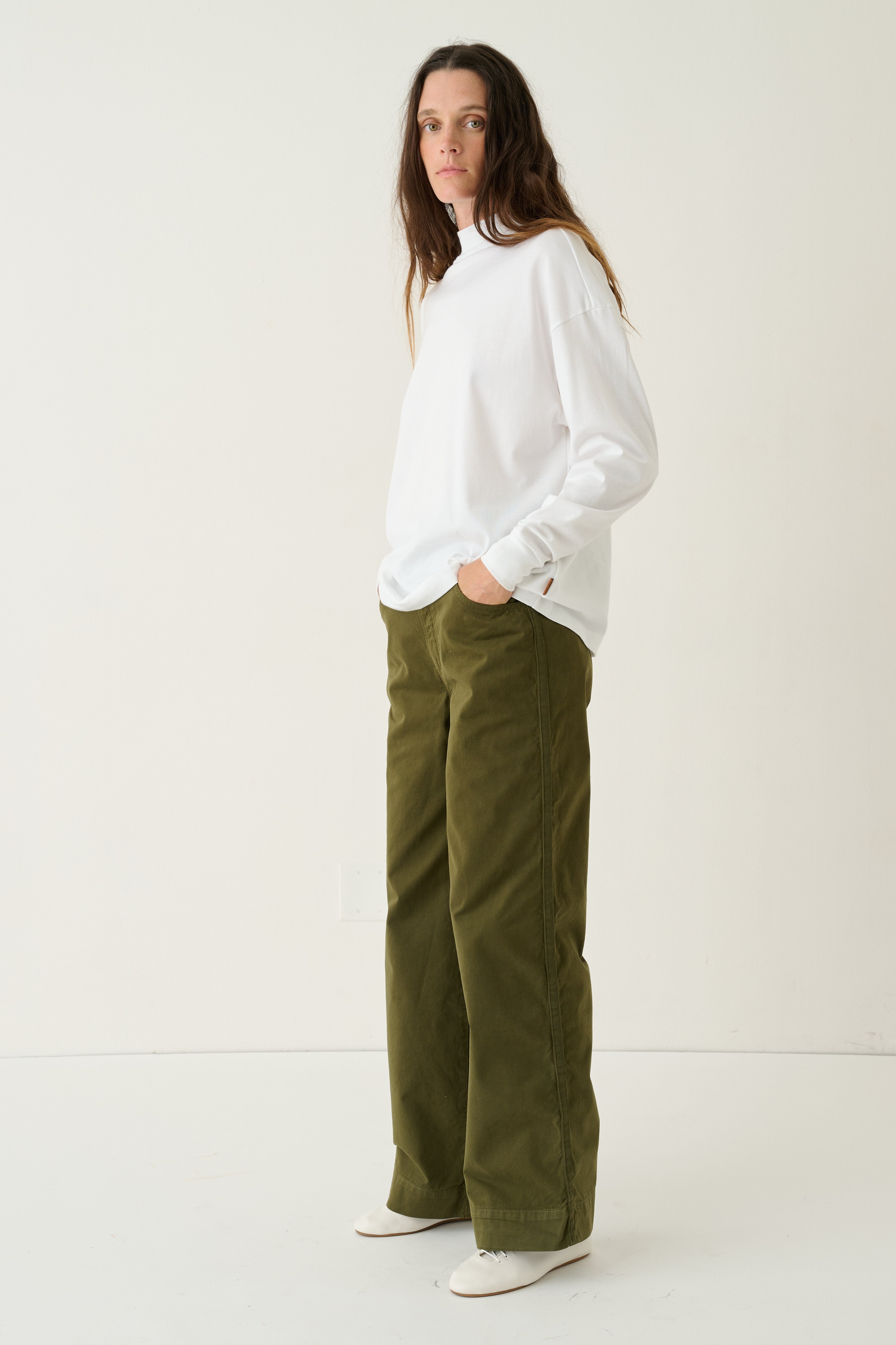 A woman modeling a white long-sleeve top and olive green wide-leg pants against a plain white studio background.