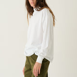 A woman modeling a white long-sleeve top with voluminous balloon sleeves and olive green trousers, standing against a plain off-white studio background.