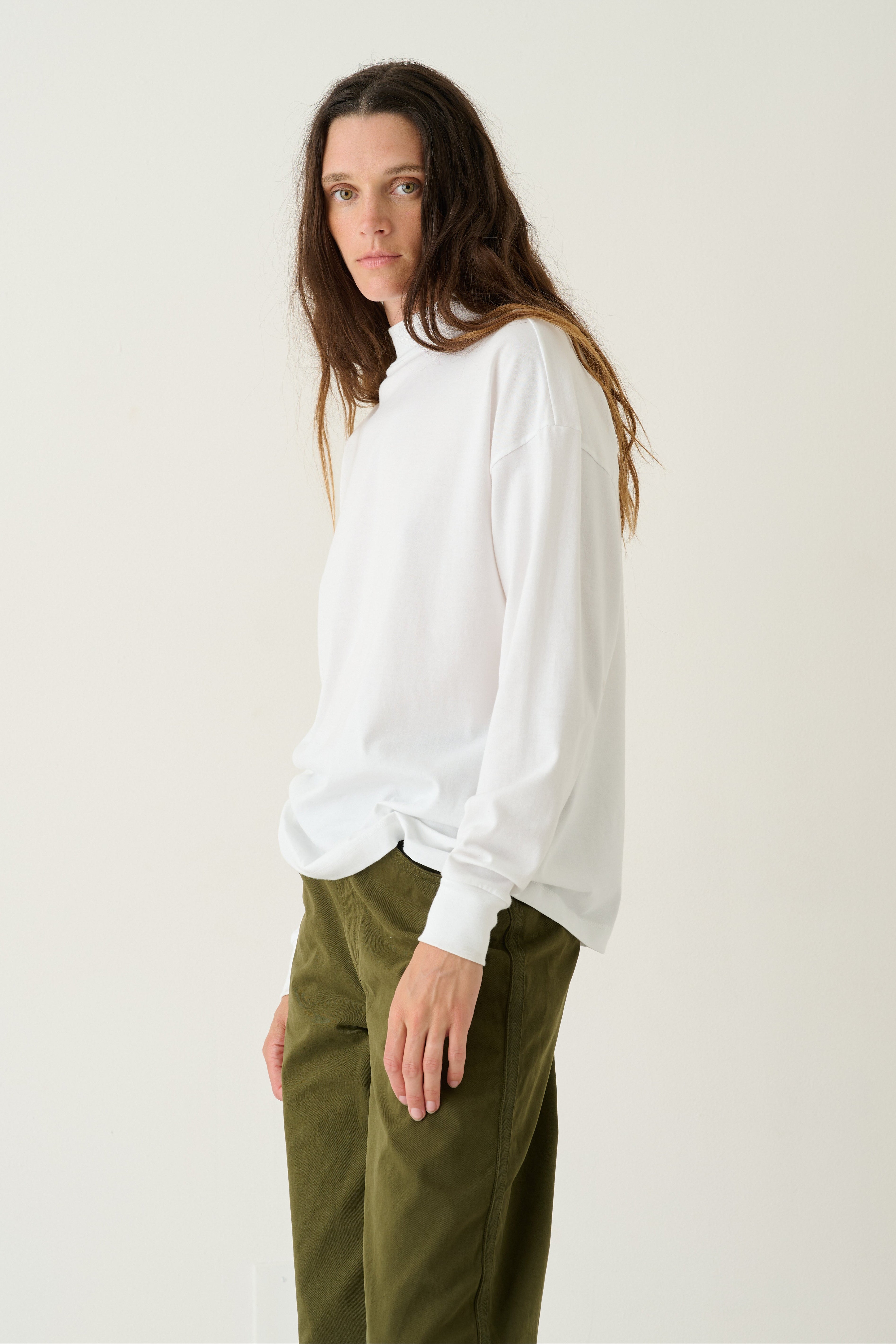 A woman modeling a white long-sleeve top with voluminous balloon sleeves and olive green trousers, standing against a plain off-white studio background.