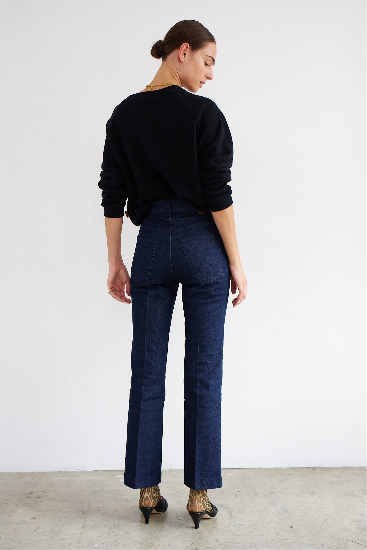 Woman wearing a black sweater and dark blue jeans against a white background