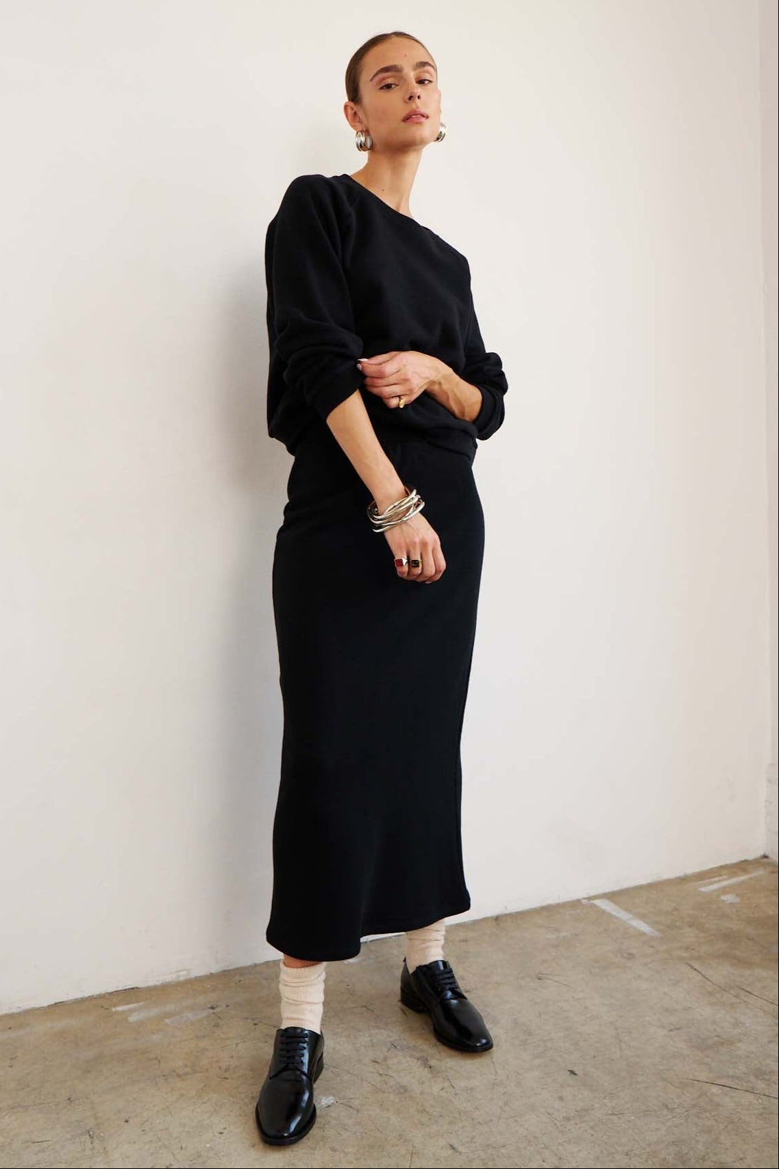 Person wearing a black outfit standing against a white wall.