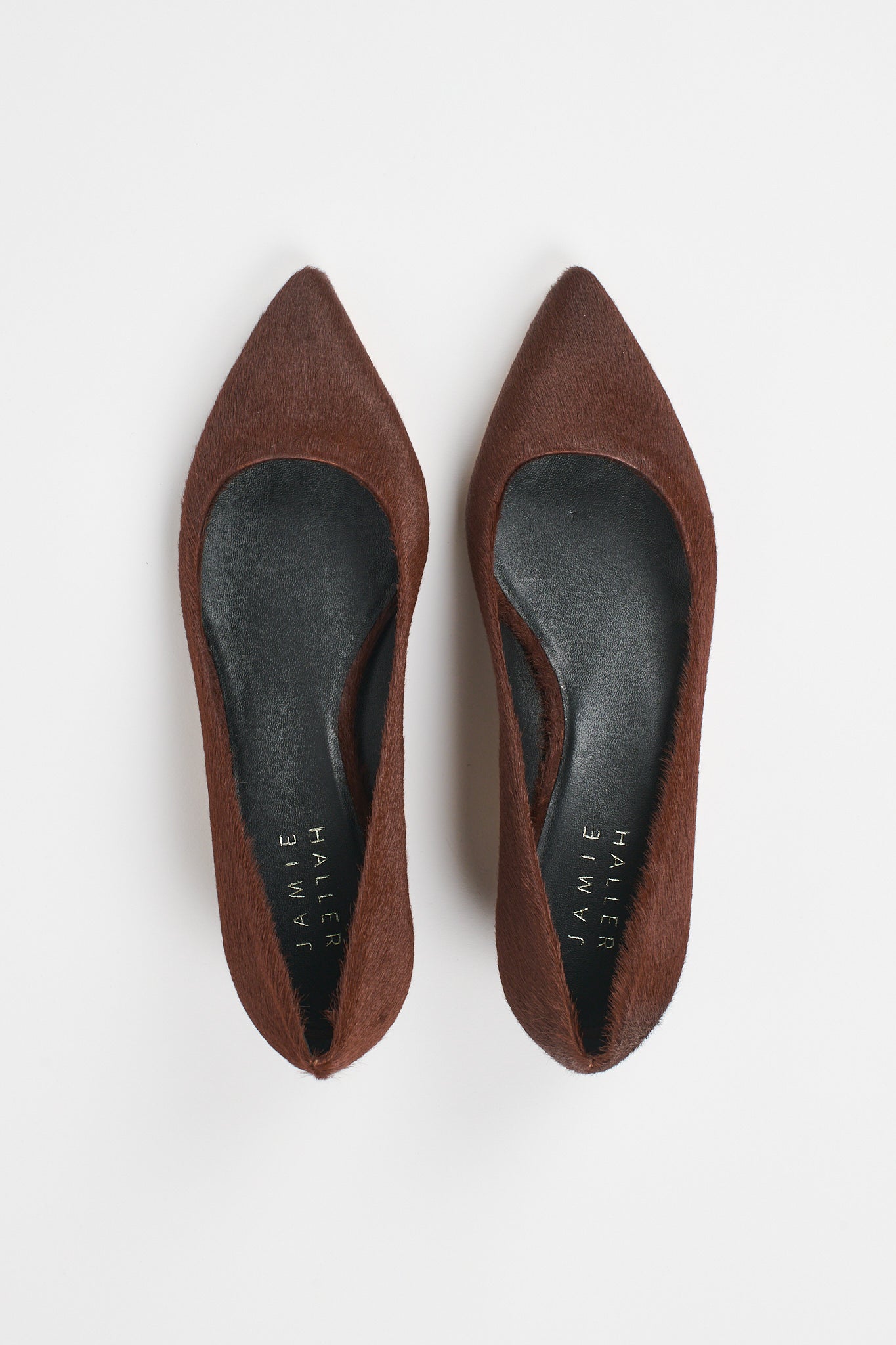 A pair of pointed-toe flat shoes in brown suede, shown from a top-down view on a light gray background. The insoles are black with the brand name 'JAMIE Haller' printed in white.