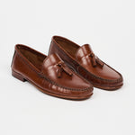 A pair of brown leather moccasin-style loafers with tassel details, photographed on a clean, light gray studio background.