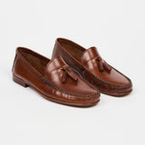 A pair of brown leather moccasin-style loafers with tassel details, photographed on a clean, light gray studio background.