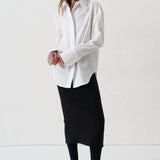 model in a white blouse, black skirt, and black heels against a white wall
