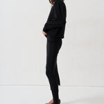 A model is shown in profile wearing a black long-sleeve top, black pants, and black-and-white zebra-patterned pointed-toe flats against a plain white studio background.