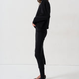A model is shown in profile wearing a black long-sleeve top, black pants, and black-and-white zebra-patterned pointed-toe flats against a plain white studio background.