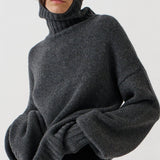 A model wearing a dark gray oversized knit turtleneck sweater, black leggings, and black-and-white striped kitten heel flats, standing against a plain white studio background.