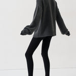 A model wearing a dark gray oversized knit sweater, black leggings, and black pointed-toe slingback heels, captured from a side-back angle against a clean white studio background.
