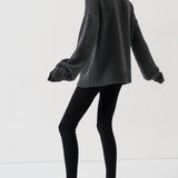 A model wearing a dark gray oversized knit sweater, black leggings, and black pointed-toe slingback heels, captured from a side-back angle against a clean white studio background.