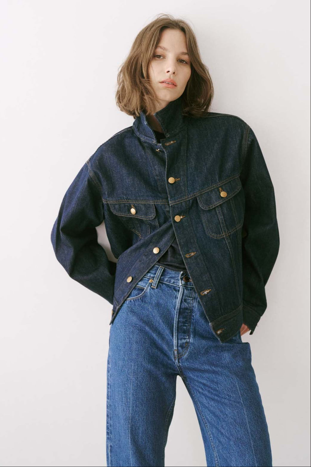 Person wearing a dark denim jacket and blue jeans against a white background