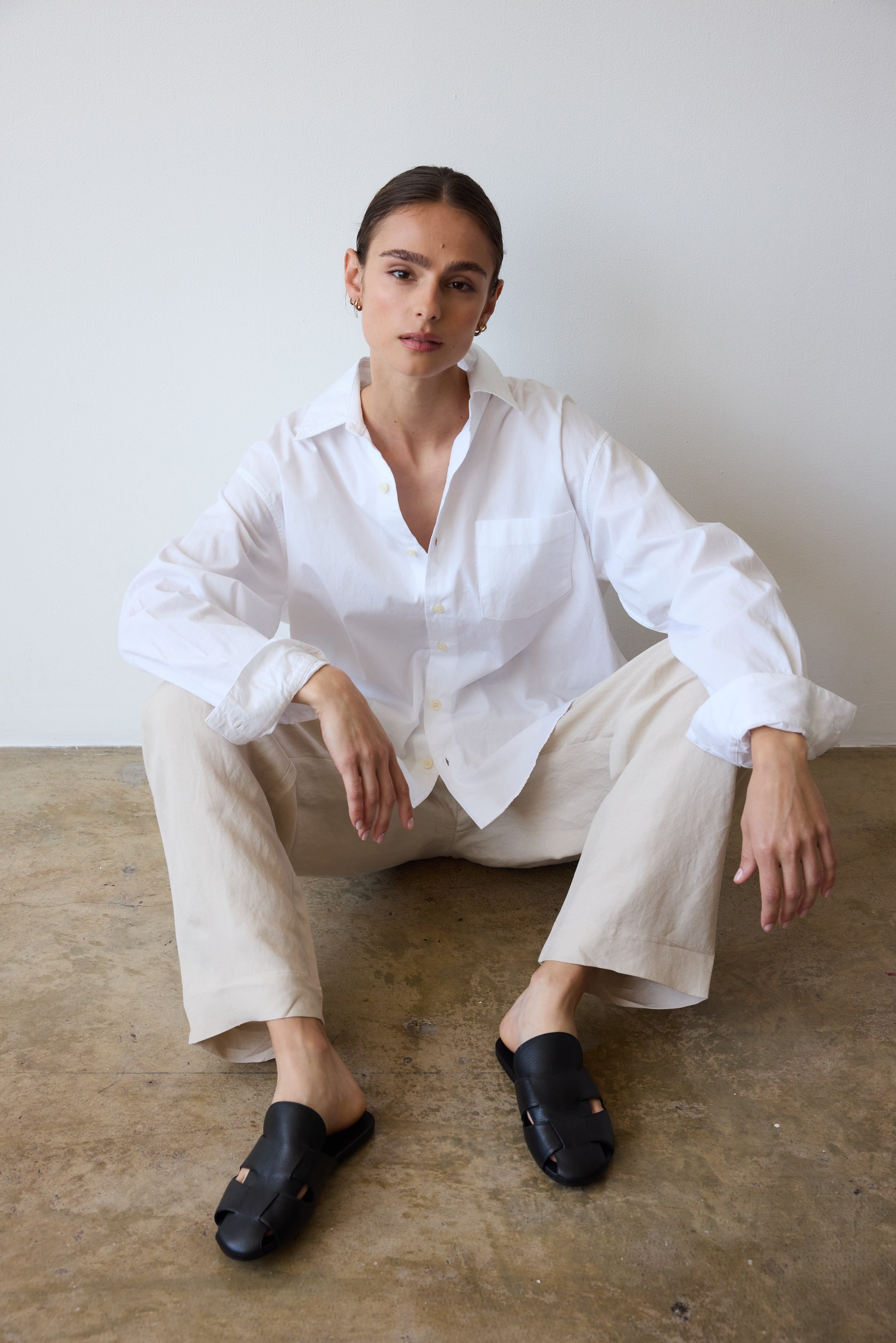 Person wearing a white shirt and beige pants sitting on a concrete floor.