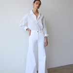 Person wearing a white outfit standing against a plain wall.