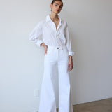 Person wearing a white outfit standing against a plain wall.