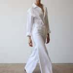 Woman wearing a white shirt and pants against a plain background