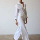 Woman wearing a white shirt and pants against a plain background