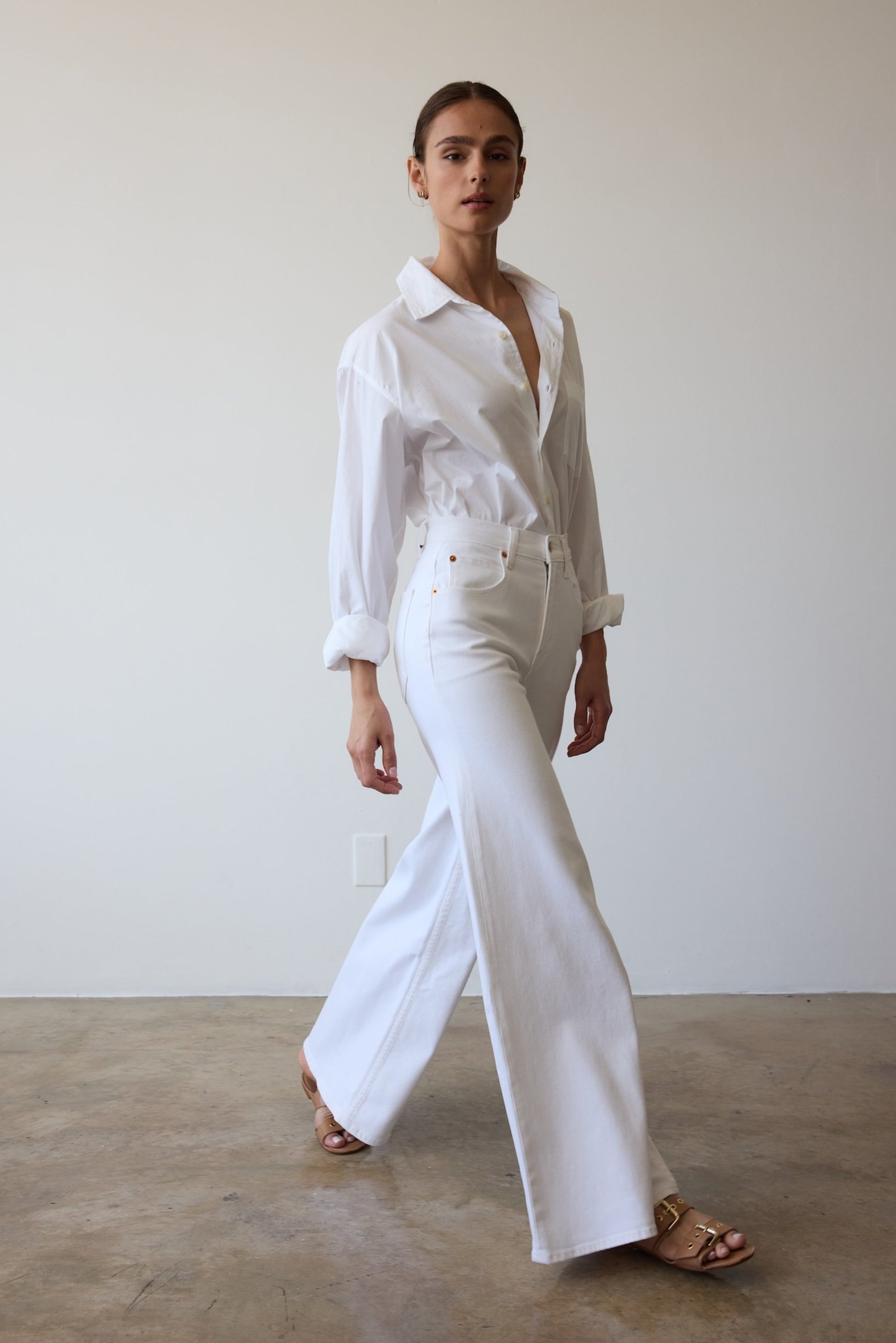 Woman wearing a white shirt and pants against a plain background