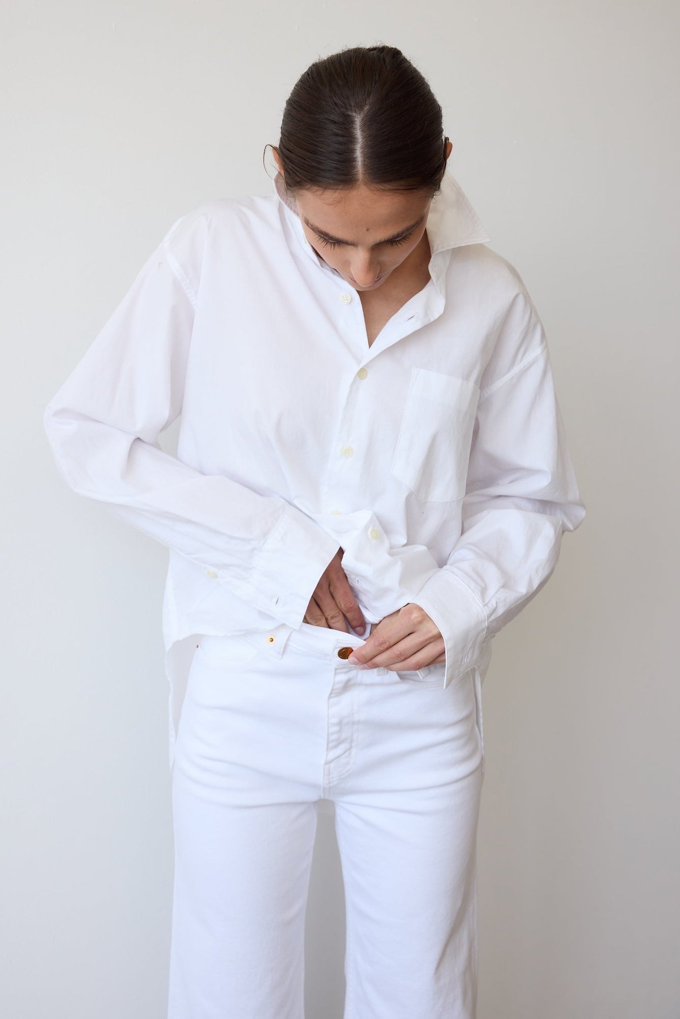 Person wearing a white shirt and white pants against a plain background