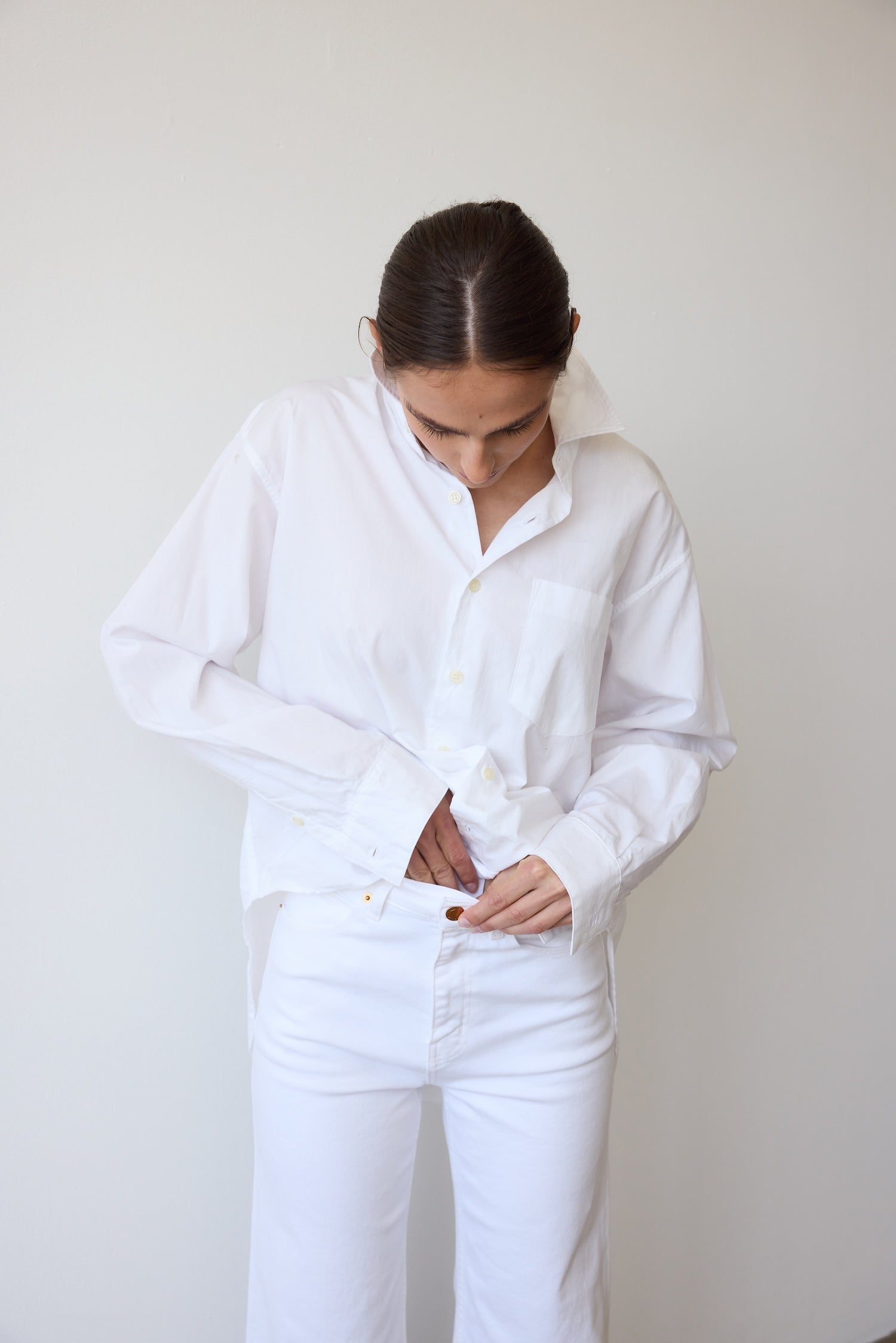 Person wearing a white shirt and white pants against a plain background