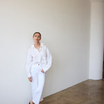 Person wearing a white outfit standing against a plain wall.