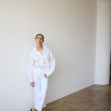 Person wearing a white outfit standing against a plain wall.
