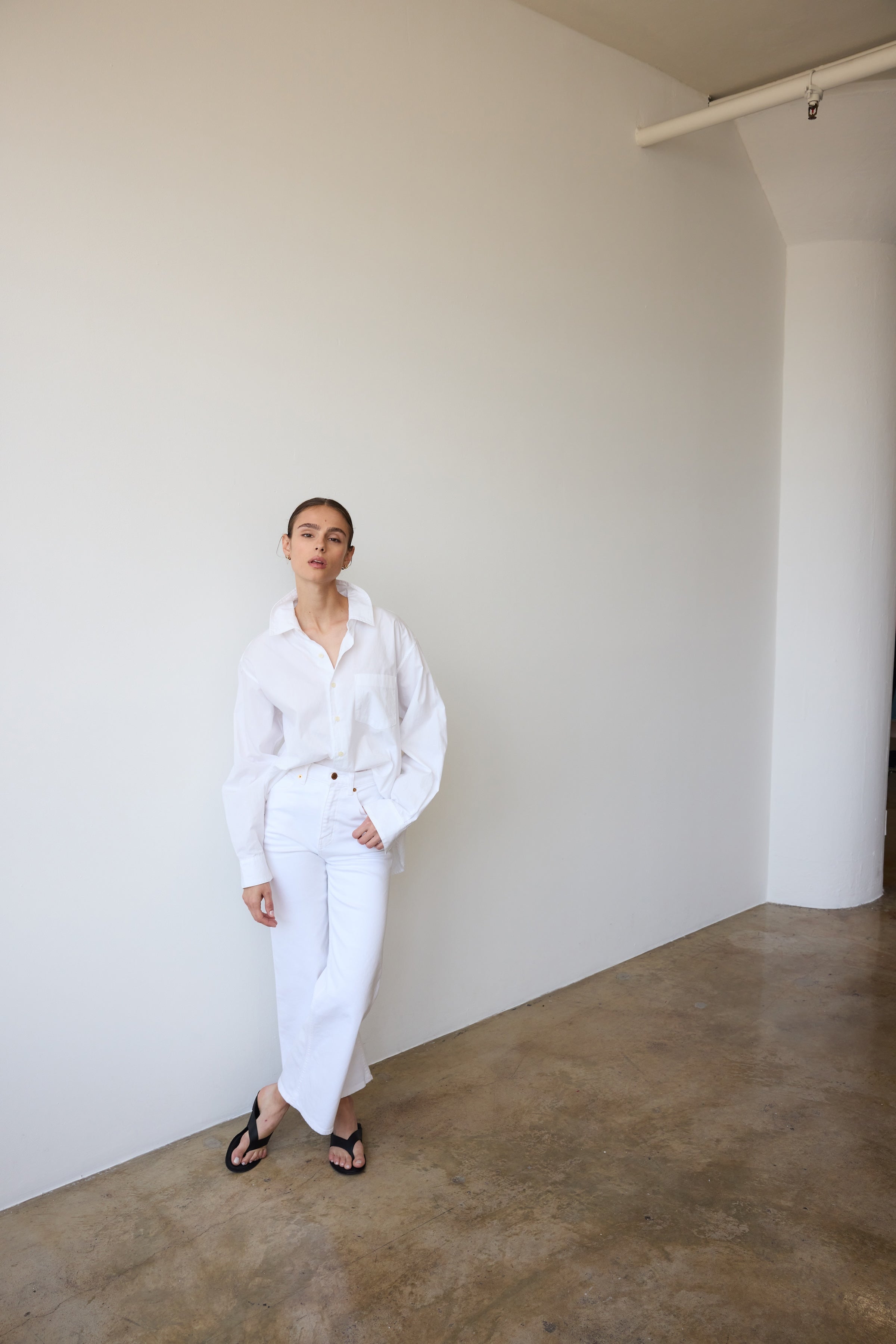 Person wearing a white outfit standing against a plain wall.