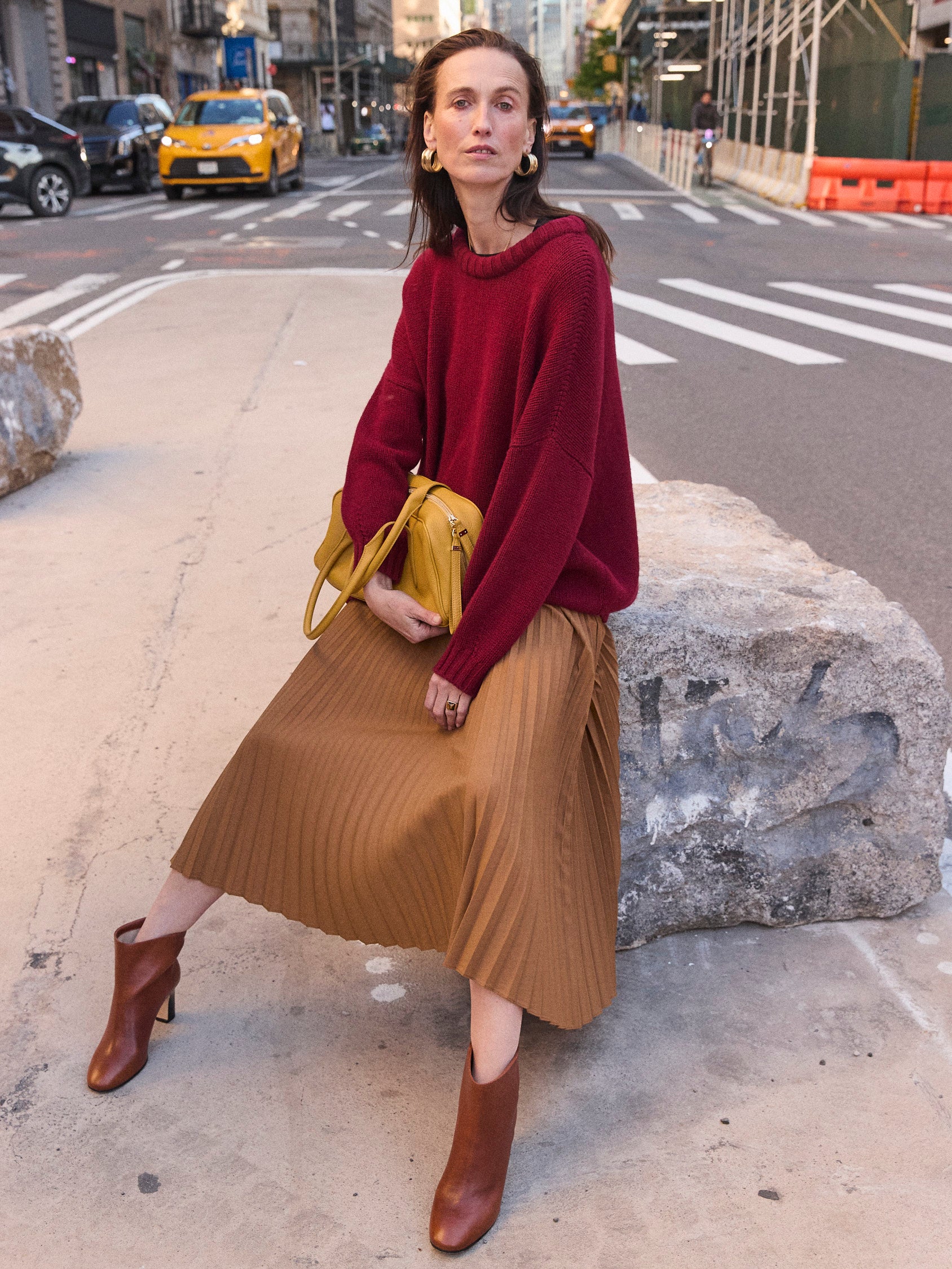 a woman sitting on a rock in the street wearing a red sweater