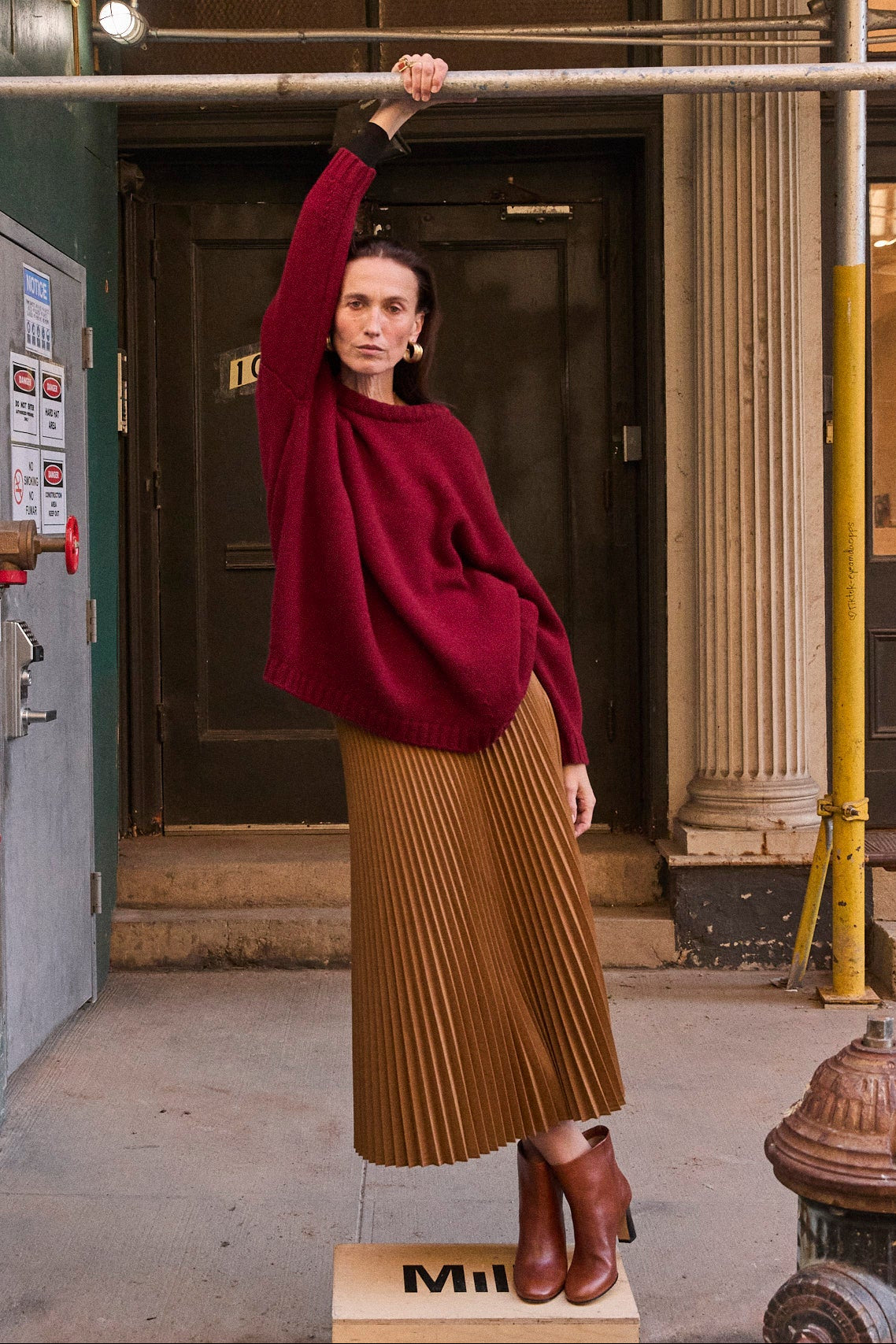 a woman in a read sweater standing on a box on the sidewalk
